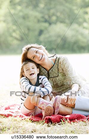 Stock Image - Mother and daughter laughing on blanket. Fotosearch