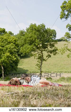 Stock Image - Mother and daughter lie on red blanket. Fotosearch