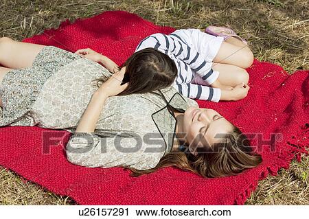Stock Image - Mother and daughter lie on red blanket. Fotosearch