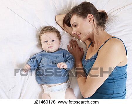 Mother lying next to baby on bed View Large Photo Image Stock Photo - Mother lying next to baby on bed. Fotosearch