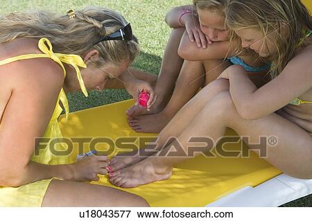 Stock Photo - Mother painting toenails of two girls. Fotosearch