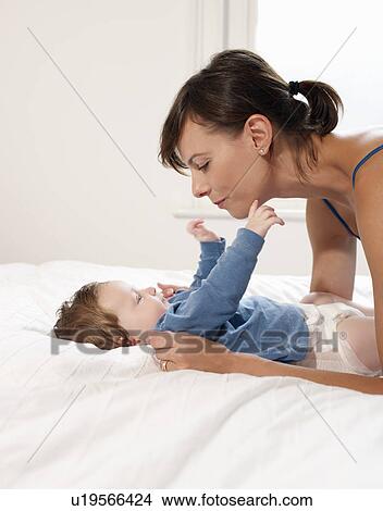Mother smiling at baby lying on bed View Large Photo Image Picture - Mother smiling at baby lying on bed. Fotosearch