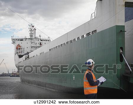 Stock Image - Port Worker Looking At Container Ship. Fotosearch