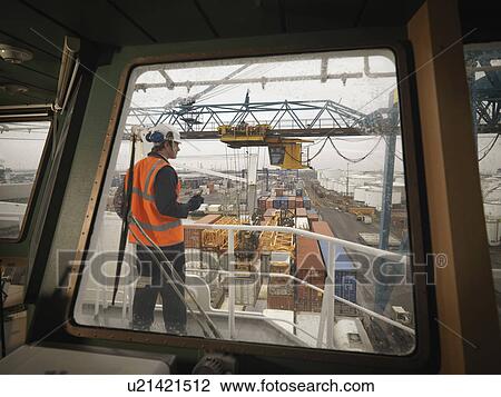 Stock Image - Port Worker Overseeing Loading Of Ship. Fotosearch
