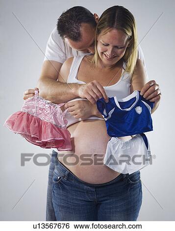 Stock Photograph - pregnant man and woman with baby clothes. Fotosearch