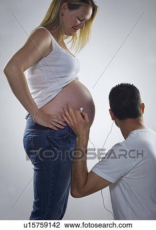 Stock Image - pregnant woman man listens on headphones. Fotosearch