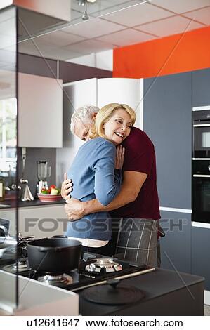 Stock Photo - Senior Couple Hugging in Kitchen. Fotosearch