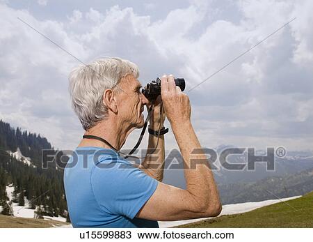 Stock Image - senior man with binoculars in mountains. Fotosearch