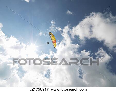 Stock Photo - Senior paraglider in midair against sky. Fotosearch