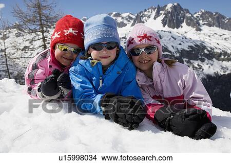 Picture - Three kids lying in the snow.. Fotosearch