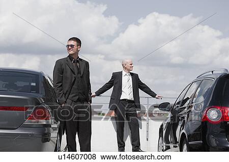 Stock Photo - two business men standing between cars. Fotosearch