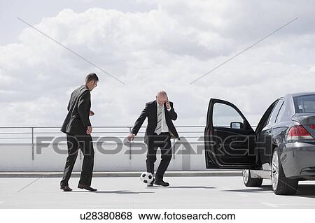 Stock Photo - two men playing football near car. Fotosearch