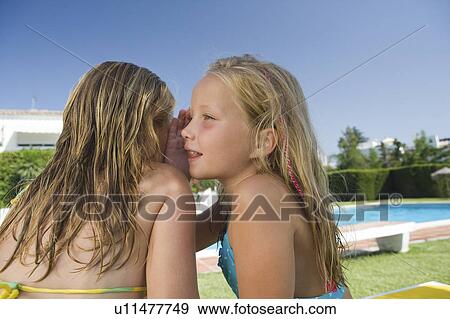 Two young girls sharing a secret by pool View Large Photo Image Stock Photo - Two young girls sharing a secret by pool. Fotosearch