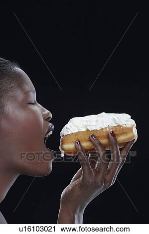 Stock Image - Woman eating cream doughnut. Fotosearch