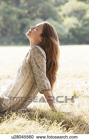 Stock Image - Woman lying back relaxing in field. Fotosearch