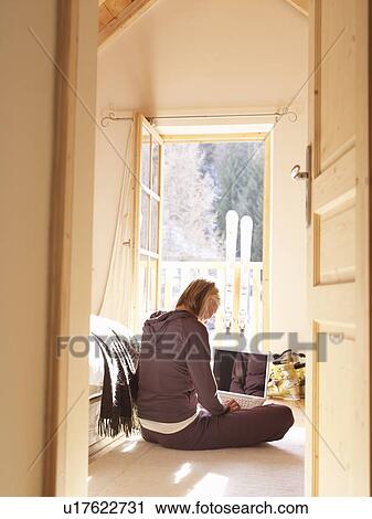 Stock Image - woman on laptop in bedroom of chalet. Fotosearch