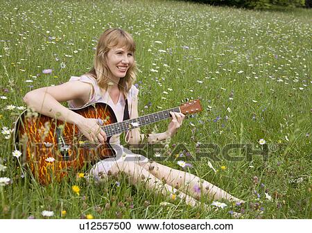 Stock Image - woman playing guitar in meadow. Fotosearch