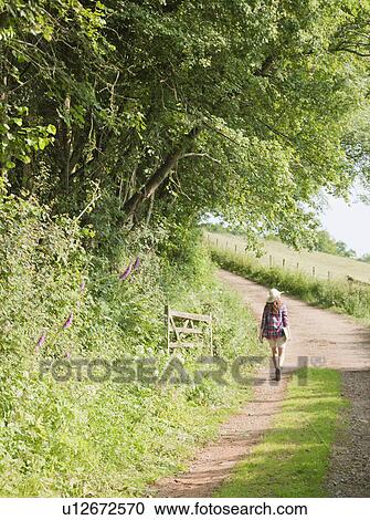 Stock Image - Woman walking down country lane. Fotosearch
