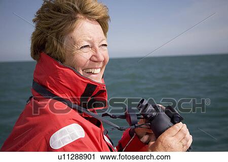 Stock Image - Woman with binoculars by ocean. Fotosearch