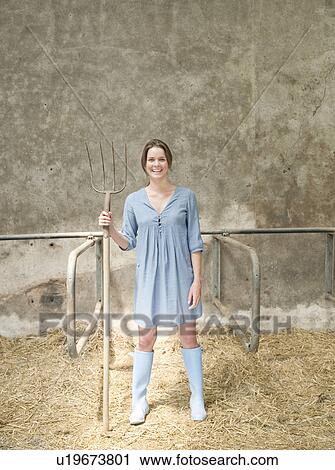 Stock Image - Woman with pitchfork in cattle shed. Fotosearch