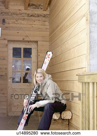 Stock Image - woman with skis sitting on bench. Fotosearch