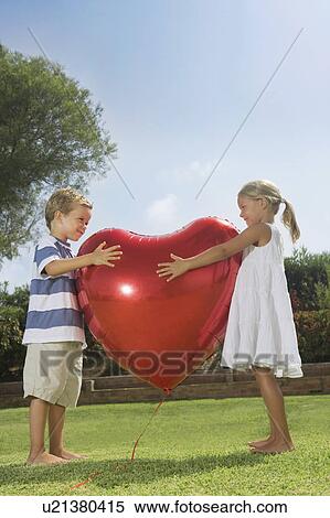 Stock Photography - Young children hugging red heart balloon. Fotosearch