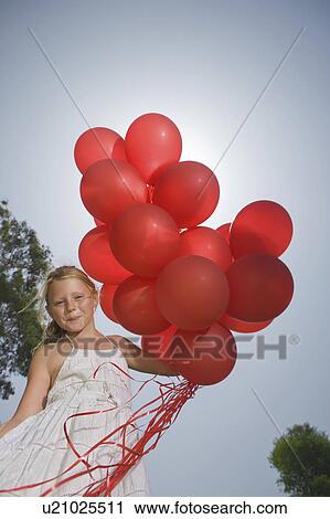 Stock Image - Young girl holding bunch of red balloons. Fotosearch