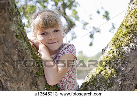 Stock Image - Young girl sitting in tree. Fotosearch