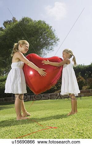 Young girls hugging red heart balloon View Large Photo Image Stock Photograph - Young girls hugging red heart balloon. Fotosearch