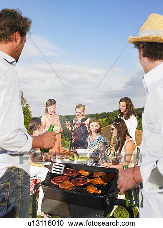 Stock Image - young men tending barbecue. Fotosearch