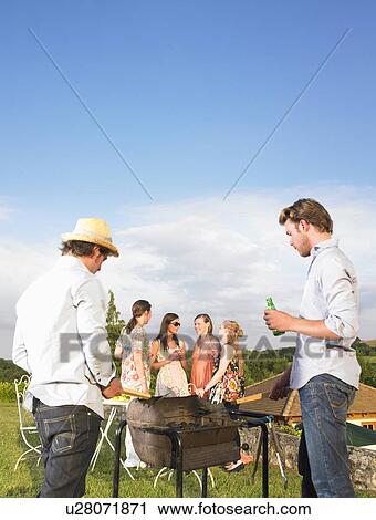 Stock Image - young men tending barbecue. Fotosearch