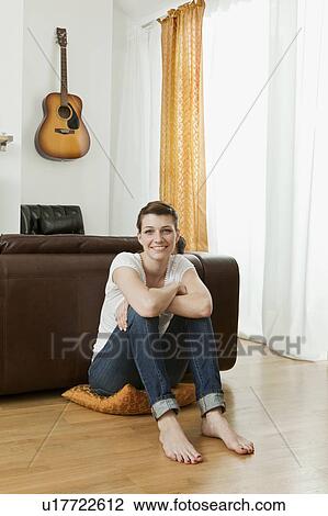 Stock Image - Young woman sitting on living room floor. Fotosearch