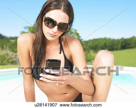 Stock Photo - young woman using phone by pool. Fotosearch