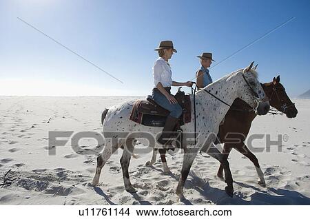 Picture - 2 people riding horses in the sand. Fotosearch