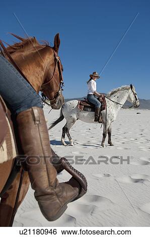 Stock Photograph - 2 people riding horses on the beach. Fotosearch