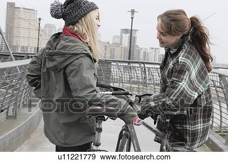 Stock Photo - 2 young women chatting with push bikes. Fotosearch