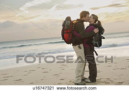 Stock Image - Backpacking couple kissing at beach. Fotosearch