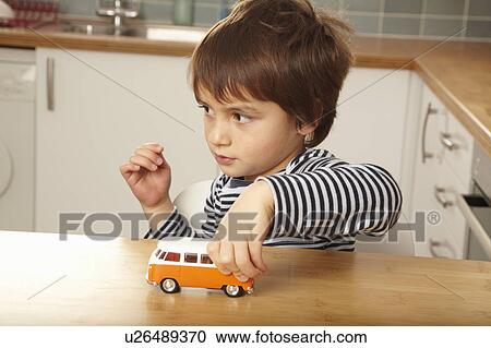 Stock Image - Boy pushing toy car on kitchen surface. Fotosearch