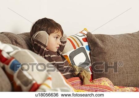 Boy sitting on sofa staring at tv View Large Photo Image Stock Photograph - Boy sitting on sofa staring at tv. Fotosearch