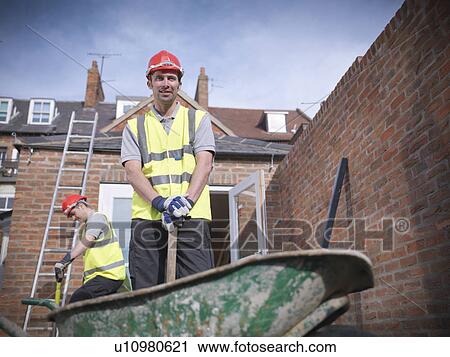 Stock Image - Builders outside house with wheelbarrow. Fotosearch