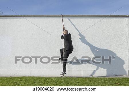 Stock Image - Businessman climbing over wall with rope. Fotosearch