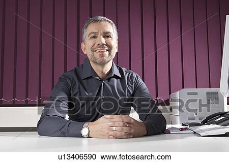 Businessman sitting at desk smiling View Large Photo Image Stock Image - Businessman sitting at desk smiling. Fotosearch
