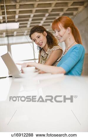Stock Photo - Businesswomen using laptop together. Fotosearch