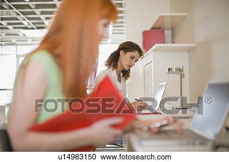Stock Image - Businesswomen using laptops in office. Fotosearch
