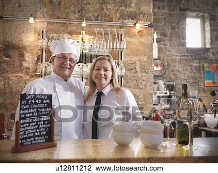 Stock Image - Chef and waitress standing behind bar. Fotosearch