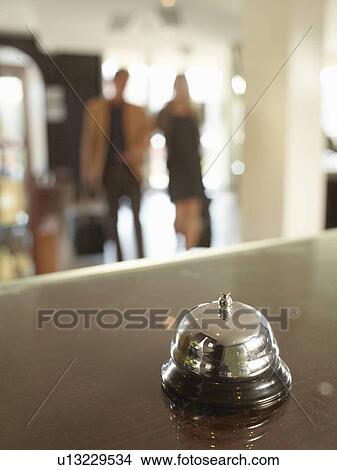 Picture - Close up of hotel porters bell with couple approaching. Fotosearch