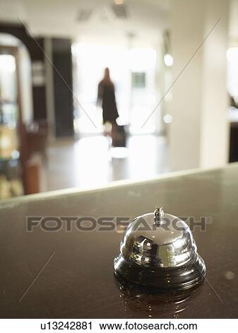 Stock Image - Close up of hotel porters bell with woman approaching. Fotosearch