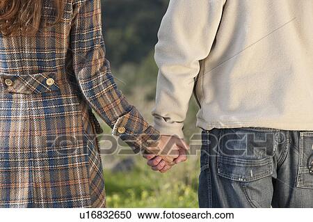 Stock Image - Close-up of young couple holding hands. Fotosearch