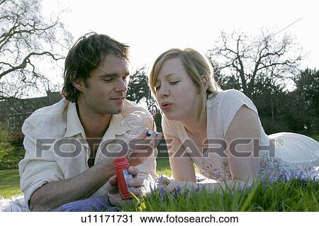 Stock Image - Couple blowing bubbles in grass at park. Fotosearch