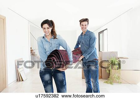 Stock Image - Couple carrying carpet in new home. Fotosearch